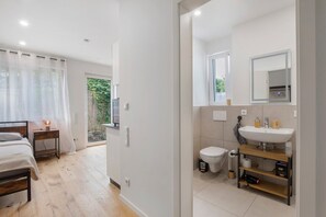 A modern bedroom with a bed, bedside table, and a view of the outside. The bathroom includes a sink, toilet, and a mirror.