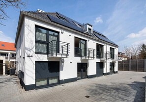 A modern two-story building with large windows, solar panels on the roof, and a gated driveway.