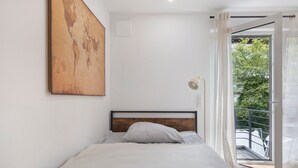 Une chambre à coucher avec un lit, une tête de lit en bois, un grand tableau abstrait, une fenêtre donnant sur un paysage verdoyant et un balcon.