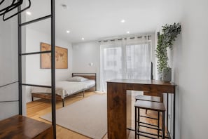 A bedroom with a bed, a desk, a chair, a window with curtains, a plant, and a world map on the wall.