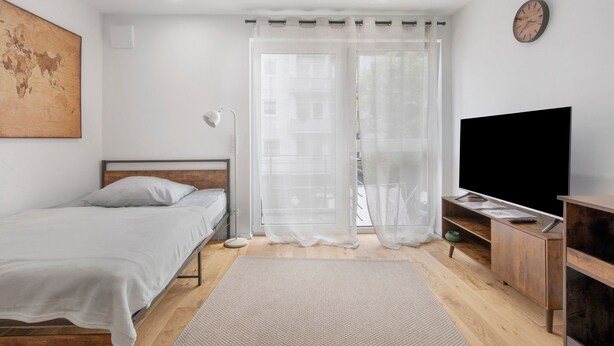 Une chambre à coucher avec un lit, une télévision, une commode en bois, un globe terrestre accroché au mur et des rideaux en voile.
