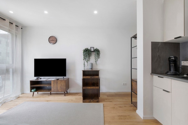 A modern living room with a flat-screen TV, wooden entertainment unit, and a small plant on a shelf.