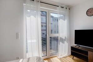 Una habitació amb una porta corredissa de vidre, una televisió sobre un suport de fusta i un rellotge de paret.