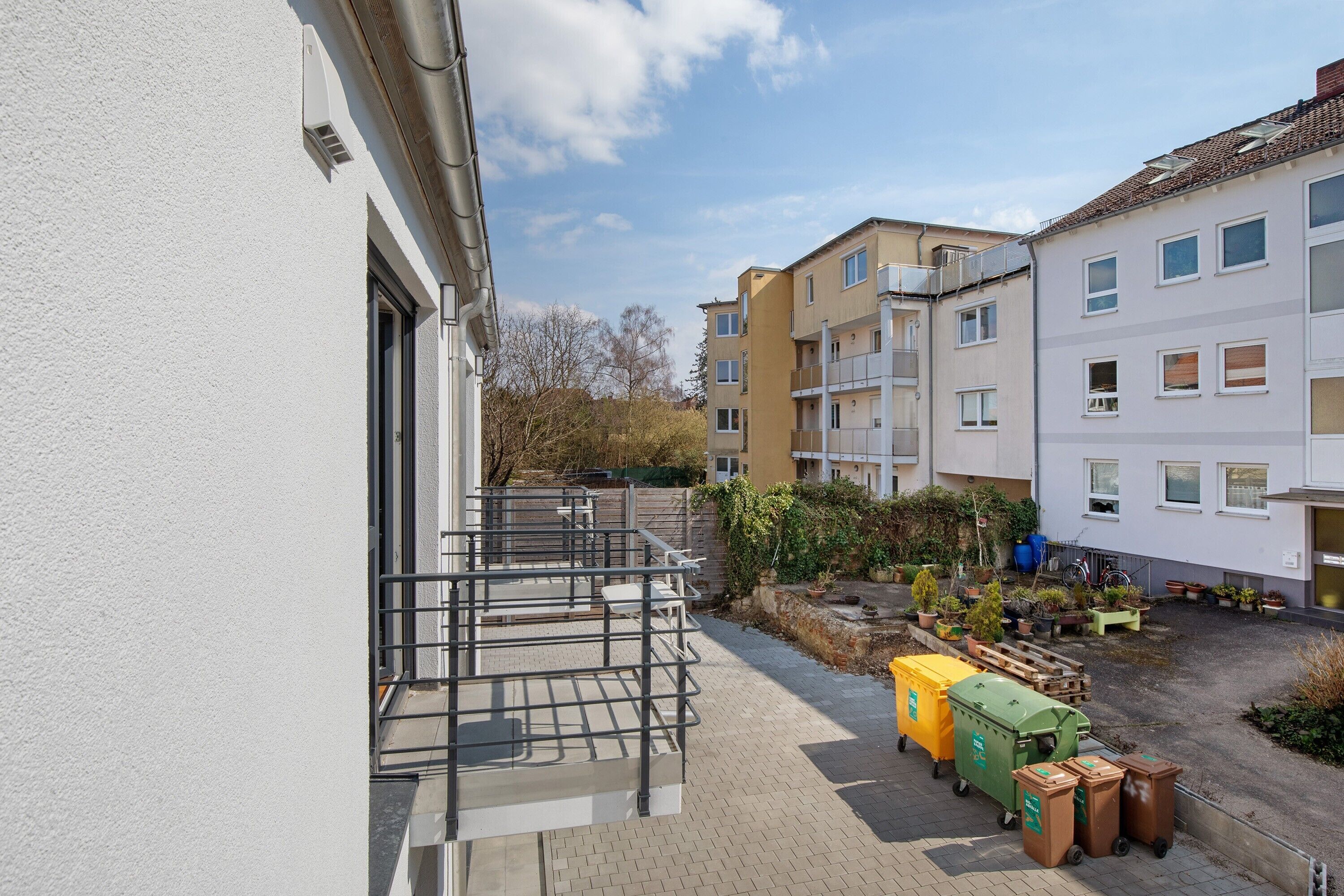 A courtyard with a building, a metal staircase, and waste bins.
