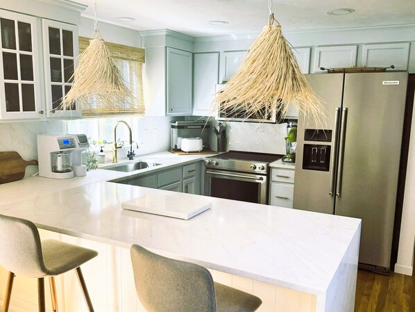 A modern kitchen with a large island, stainless steel appliances, and a hanging light fixture.