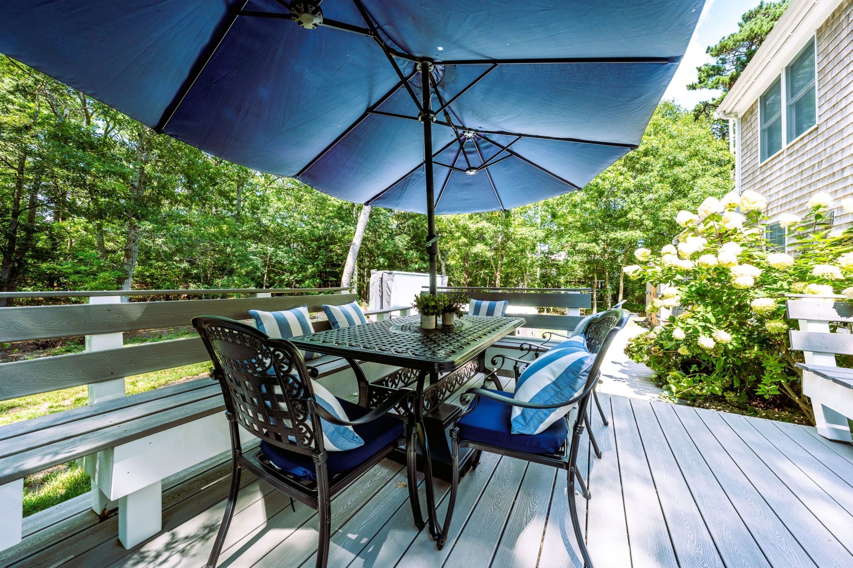 A deck with a table and chairs, surrounded by a white fence and greenery.