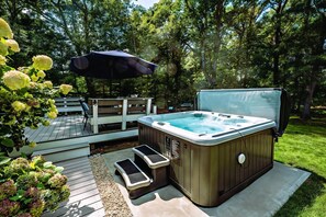 Un bain à remous avec des marches, une terrasse et un espace salon couvert avec un parasol.