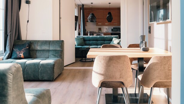 Ein modernes Wohnzimmer mit einem grünen Sofa, einem Holzesstisch und beigen Stühlen.