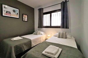 Une chambre avec deux lits, une fenêtre avec des rideaux, un tableau accroché au mur et une lampe de chevet.