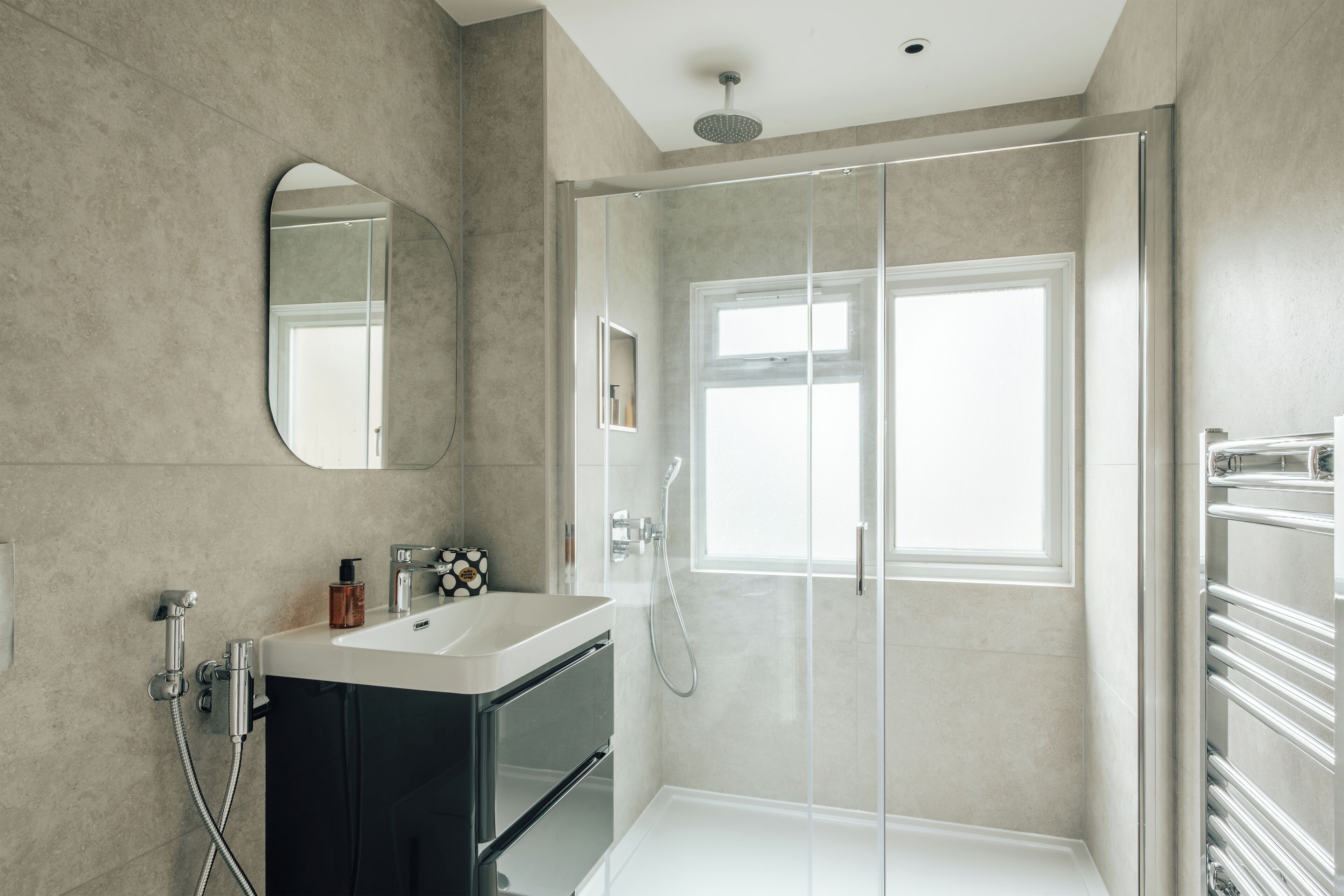 Un bany modern amb una cabina de dutxa de vidre, un mirall gran i un lavabo amb prestatge.