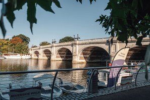 Ein Uferweg mit einer Steinbrücke im Hintergrund.