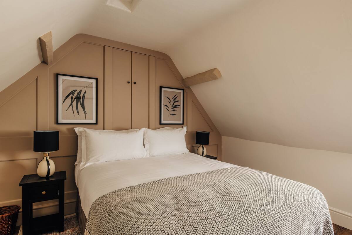Une chambre avec un plafond en pente, deux œuvres d’art encadrées accrochées au mur, un lit avec une literie blanche et deux lampes de chevet.