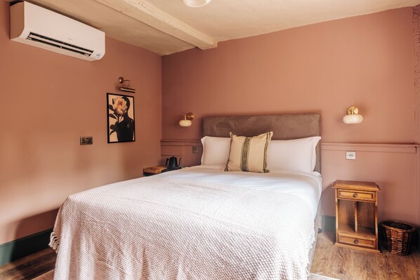 A bedroom with a large bed, a nightstand, a wall-mounted air conditioner, and a framed picture on the wall.