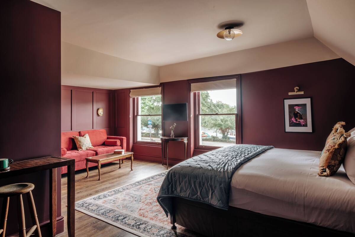 Une chambre à coucher avec un lit, un canapé rouge, une petite table et une fenêtre.