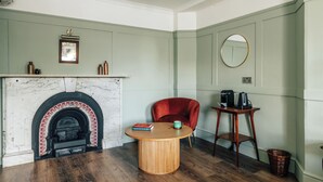 A room with a fireplace, a round wooden table, a red chair, and a small side table with a kettle. - Hermes Hotel by Nestor (Kingston Upon Thames)