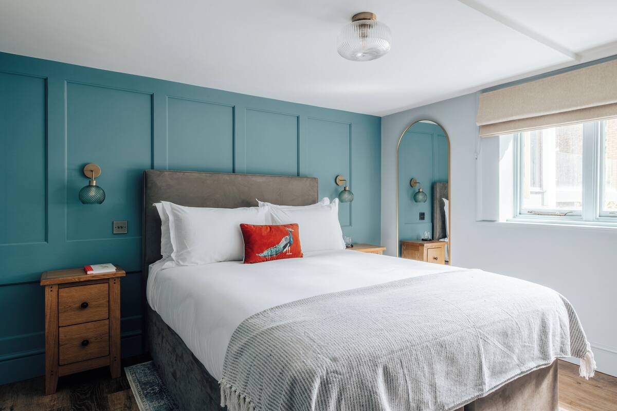 Une chambre avec un grand lit, une table de chevet, une commode, un miroir et une fenêtre donnant sur un beau paysage.
