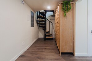 Una escalera con acabado de madera, un aparador de madera con cajones y una planta colgante.