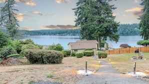 A lakeside property with a pathway leading to a house, surrounded by dense greenery and a wooden fence. - Oceanfront boho cottage in Bremerton (Bremerton)