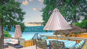 A deck with outdoor furniture, a table, and a view of a lake. - Oceanfront boho cottage in Bremerton (Bremerton)
