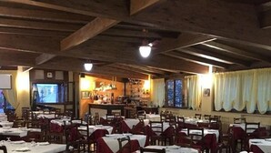 Un restaurante con vigas de madera, mesas dispuestas con manteles blancos y una barra visible al fondo.