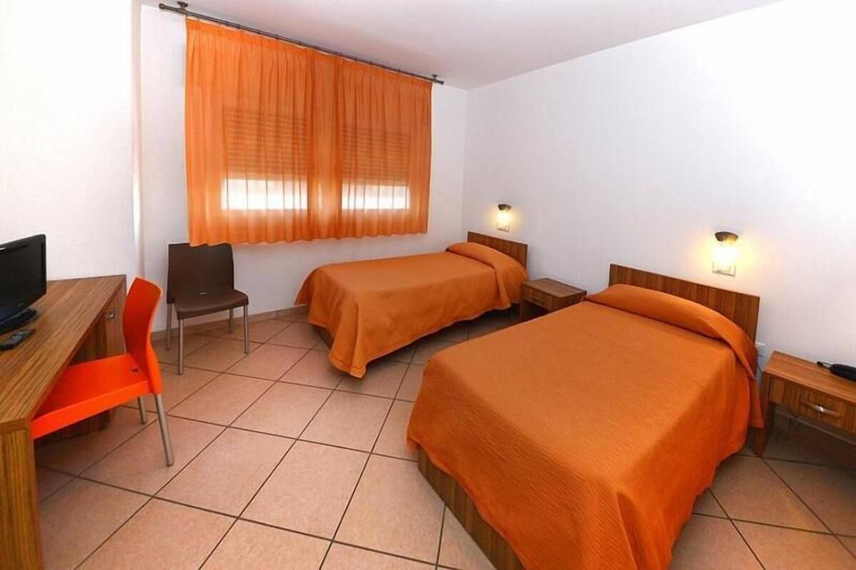Habitación de hotel con dos camas, un escritorio, una silla y dos mesitas de noche con lámparas.