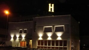 Un edificio con un letrero grande con la letra 'H', amplias ventanas y un estacionamiento.
