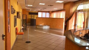 Un vestíbulo amplio con una recepción, un área de espera con sillas y un suelo de baldosas.