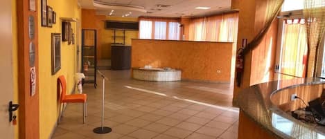 Un hall d’entrée spacieux avec un comptoir de réception, un espace d’attente doté de chaises et un sol carrelé.