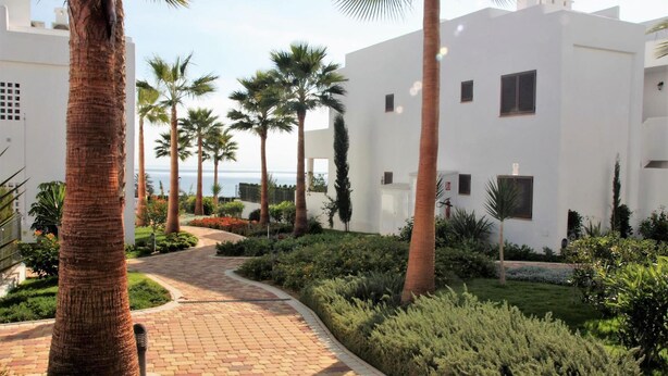 A pathway leading to a white building with multiple windows, surrounded by palm trees and well-maintained greenery. - Lorandalou - Two Bedroom Apartment, Sleeps 4 (San Juan de los Terreros)