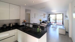 A modern kitchen with a black countertop, white cabinets, and a dining area with a sofa and coffee table. - Lorandalou - Two Bedroom Apartment, Sleeps 4 (San Juan de los Terreros)