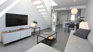 Un salon moderne avec un téléviseur à écran plat, un canapé, une table basse et un escalier.