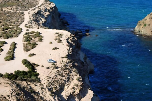 A coastal landscape with a narrow sandy path leading to a cliff edge overlooking the sea.