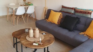 Een moderne woonkamer met een grijze bank, een ronde salontafel en een eethoek met een witte tafel en stoelen.