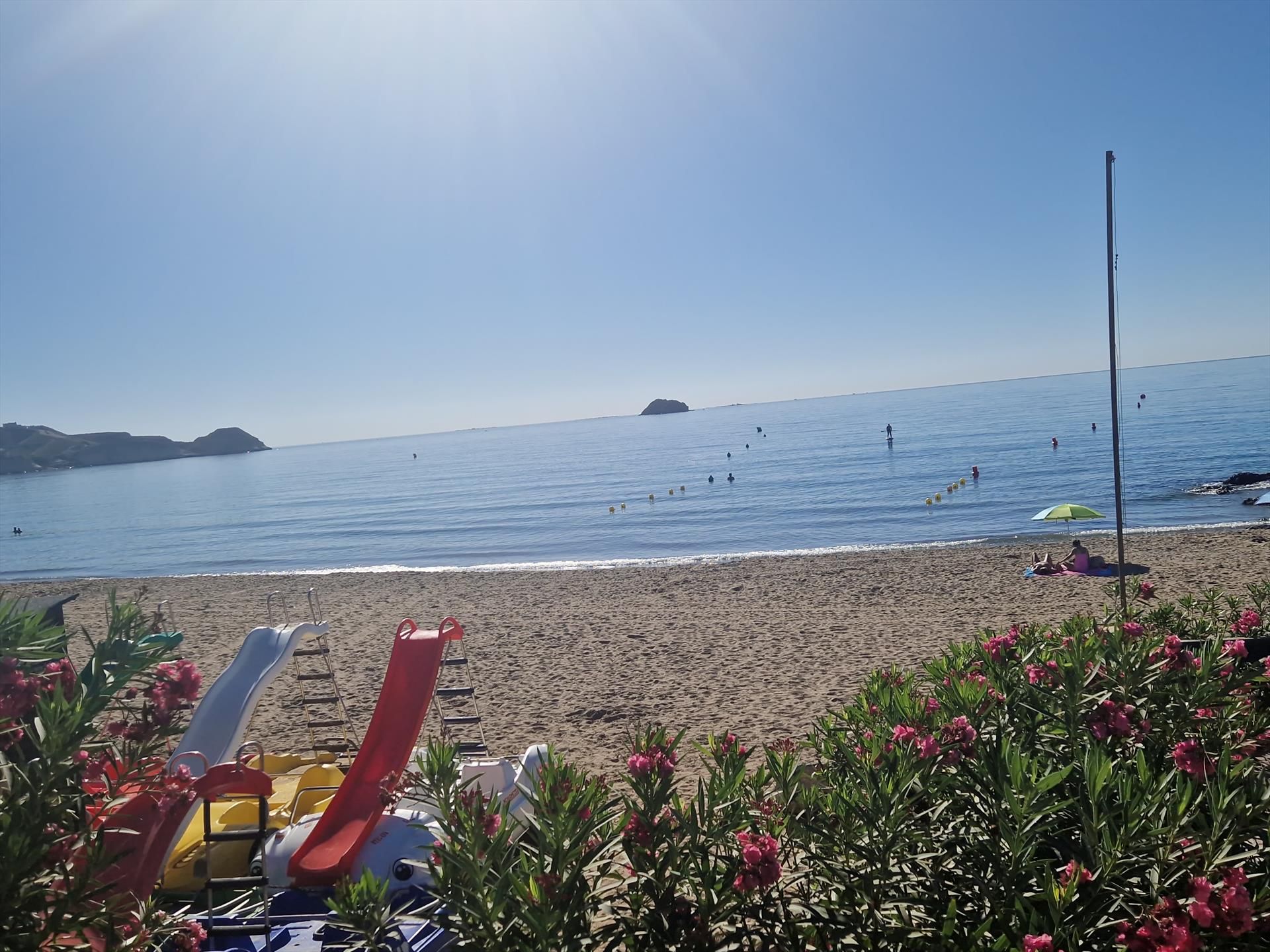 A beach with a clear sky, a sandy shore, and a few people in the water.