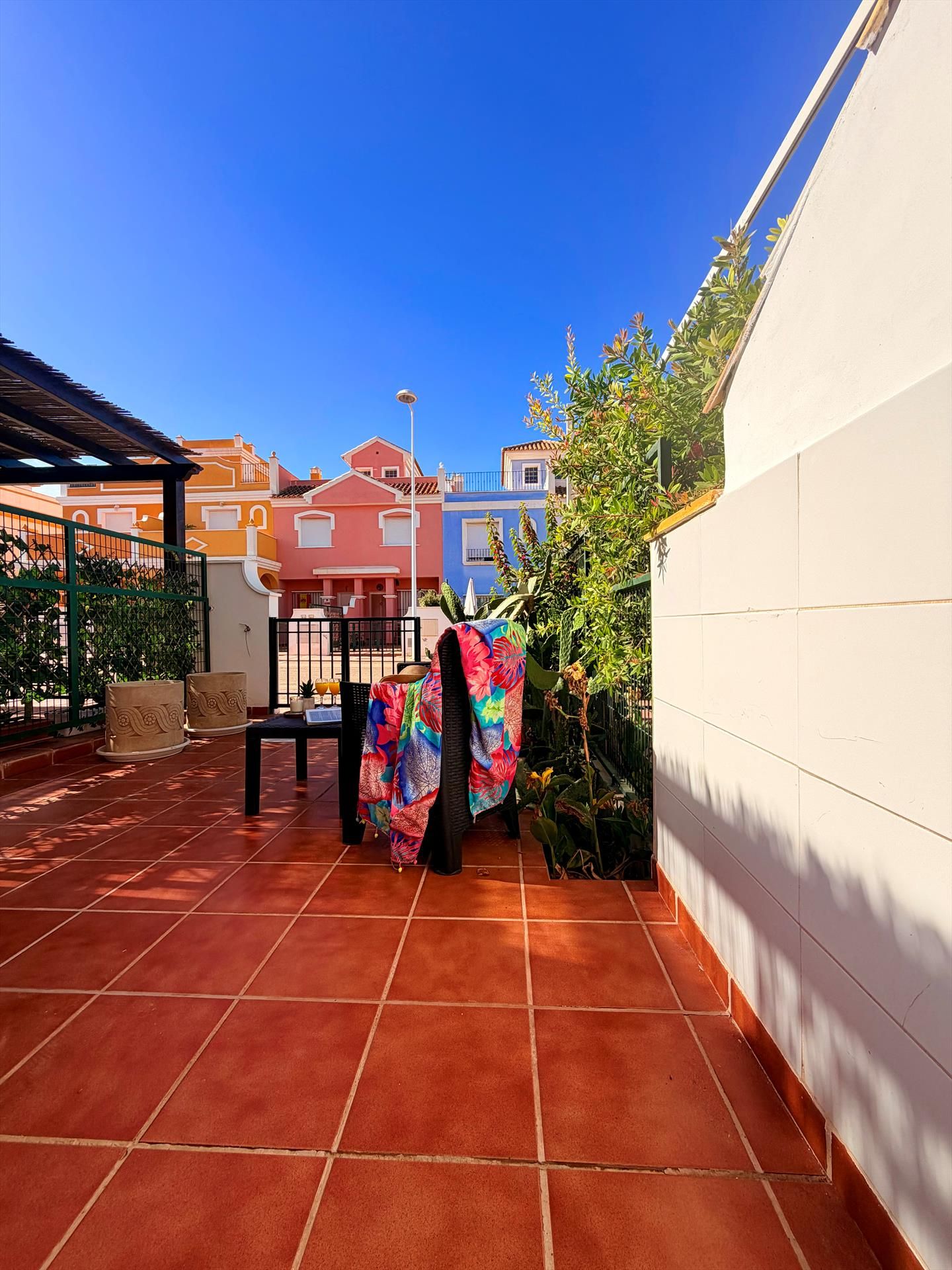 Een terras met terracotta tegels, een witte muur en een kleurrijke parasol.