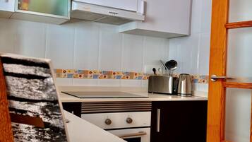 Una cocina con armarios blancos, estufa, tostadora y hervidor.