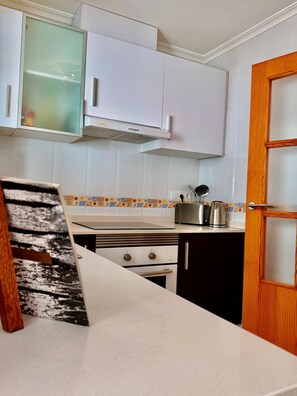 A kitchen with white cabinets, a stove, a toaster, and a kettle.