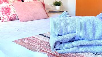 Una cama bien hecha con una toalla azul, un cojín estampado en rojo y blanco, y un cojín con motivos florales.