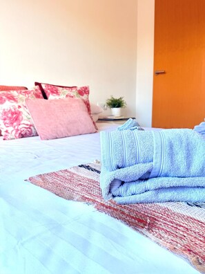 A neatly made bed with a blue towel, a red and white patterned pillow, and a floral pillow.