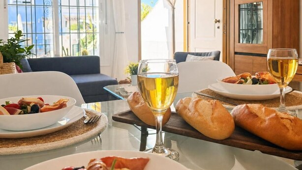 Un coin repas avec une table dressée pour deux personnes, où l’on voit un repas composé de pain, un verre de vin et une assiette de nourriture.