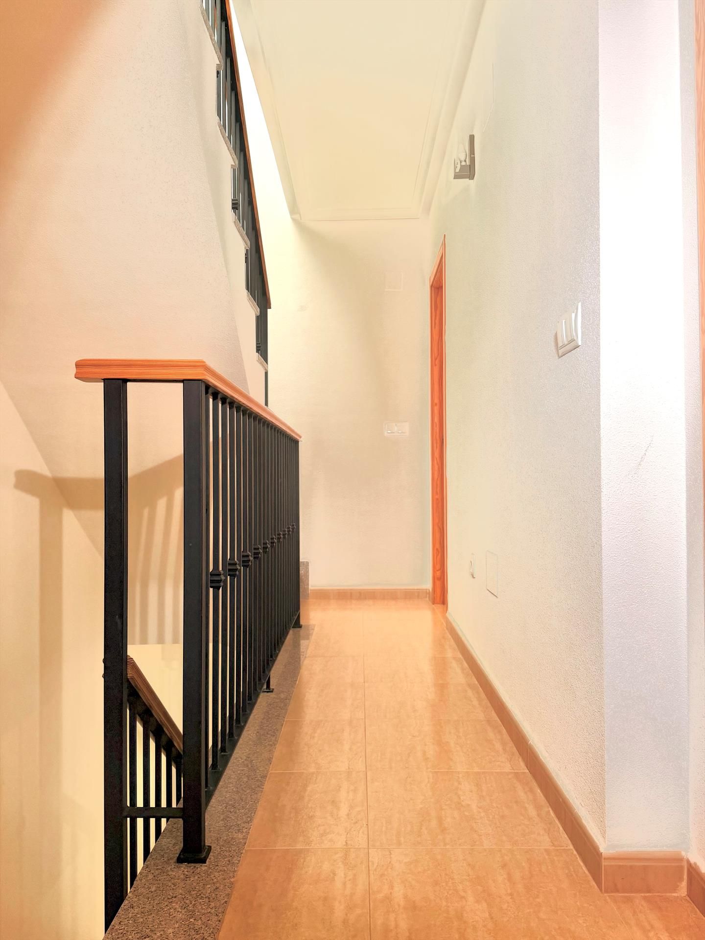 Un pasillo con barandilla de madera y pasamanos de metal negro, que conduce a una puerta al final.
