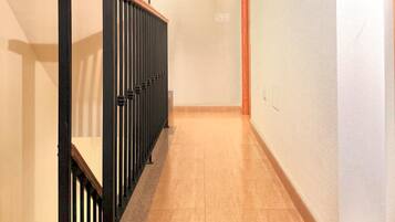 Un pasillo con barandilla de madera y pasamanos de metal negro, que conduce a una puerta al final.