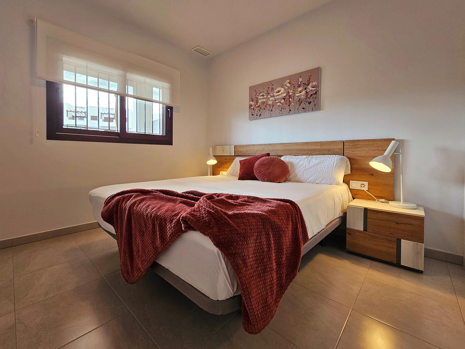 Une chambre à coucher comprenant un lit, des tables de chevet, une fenêtre et une œuvre d’art accrochée au mur.