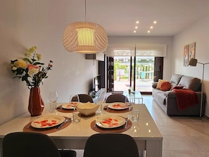 A dining area with a table set for four, a vase of flowers, and a view to the outside.