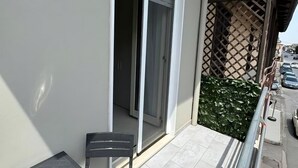 A balcony with a table and chairs, a sliding glass door, and a view of the street.