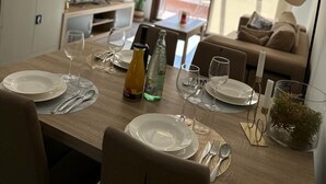 A dining area with a wooden table set for four, a hanging light fixture, and a view of a living room with a sofa and a window. - Casa Pedro - Two Bedroom Apartment, Sleeps 4 (San Juan de los Terreros)