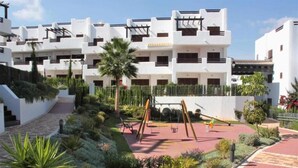 A modern building with multiple balconies and a landscaped courtyard with a swing set. - Casa Pedro - Two Bedroom Apartment, Sleeps 4 (San Juan de los Terreros)