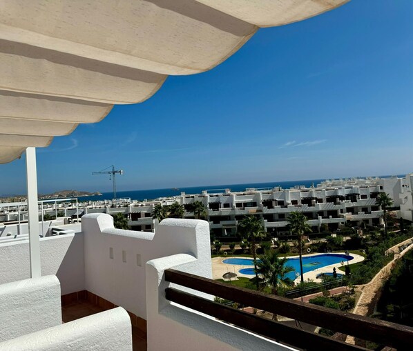 Una terraza en la azotea con piscina, edificios blancos y una vista despejada del mar.