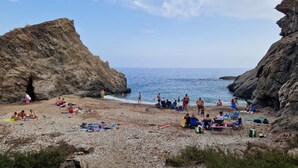 Una playa rocosa con gente tomando el sol y nadando, rodeada de acantilados.