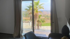 A room with a large sliding glass door leading to a balcony, two upholstered chairs, a dark wooden table, and a decorative fruit bowl. - Villa Principi di Moschitta - luxury stay in Sicily and event space (Caltagirone)